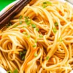 A bowl of cold sesame noodles garnished with chopped green onions, with chopsticks resting on top.