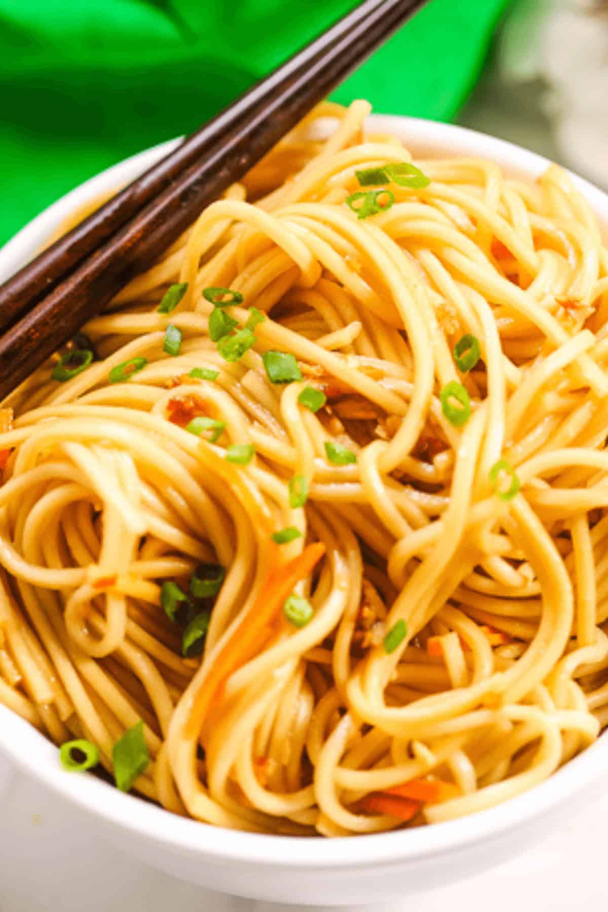 A bowl of cold sesame noodles garnished with chopped green onions, with chopsticks resting on top.
