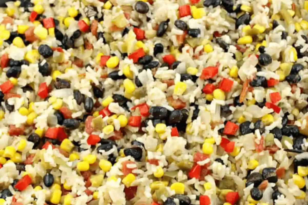 A close-up of a festive mixed rice dish, perfect for Cinco de Mayo, featuring white rice, black beans, corn, and vibrant red bell pepper pieces.