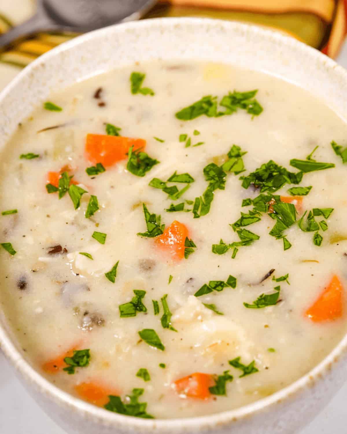 A bowl of Creamy Chicken Wild Rice Soup with vegetables and herbs.