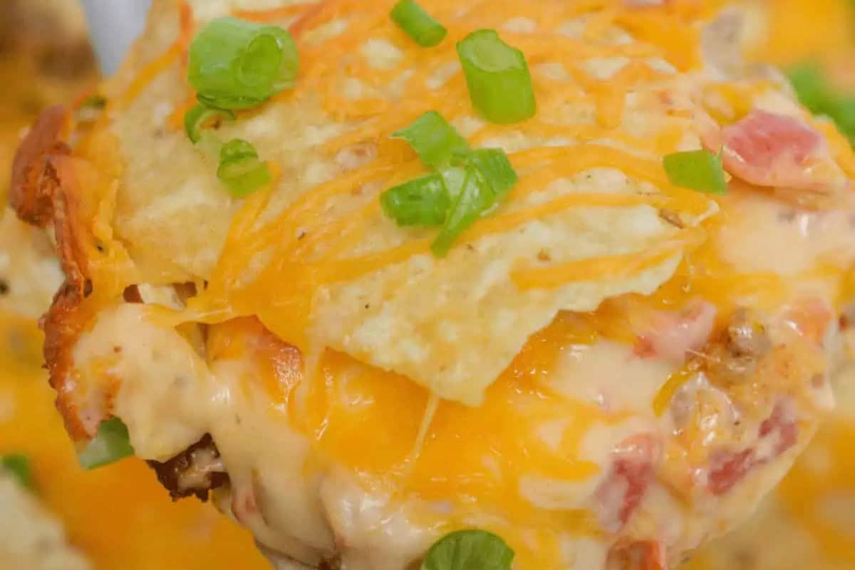 Close-up of a cheesy casserole—perfect for Cinco de Mayo celebrations—topped with crumbled chips, melted cheddar, and sliced green onions.