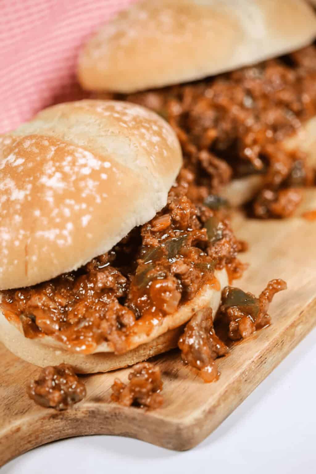 Two delicious Wimpies, also known as Easy Sloppy Joes, filled with a savory mixture of ground meat, onions, and green peppers on a wooden board.