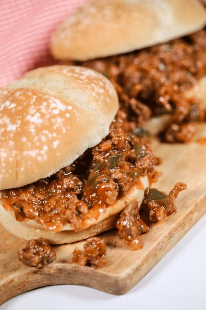 Two delicious Wimpies, also known as Easy Sloppy Joes, filled with a savory mixture of ground meat, onions, and green peppers on a wooden board.