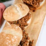 Three Wimpies (Easy Sloppy Joes) with ground meat filling on a wooden cutting board. A red checkered cloth and a green pepper are visible in the background.