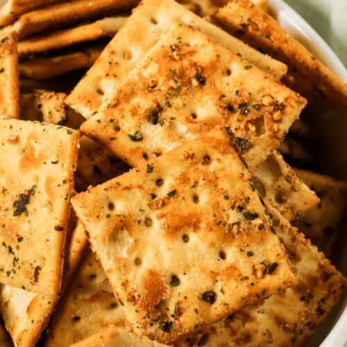 A close-up view of a bowl filled with seasoned ranch spicy crackers topped with herbs.