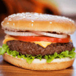 A close-up of the meal with crispy lettuce, juicy tomato, melted cheese, onion, and a beef patty in a sesame seed bun placed on a wooden surface. This mouthwatering creation showcases the art of baked hamburgers.