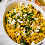 A bowl of Mexican corn salad with crumbled cheese and chopped cilantro garnish.