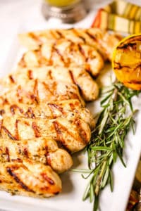 Chicken breast with rosemary on white plate with grilled lemons