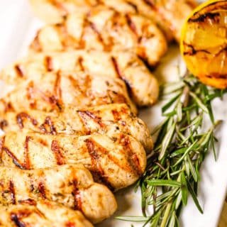 Chicken breast with rosemary on white plate with grilled lemons