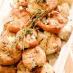 A plate of roasted smashed potatoes garnished with fresh thyme, offering a crispy texture with every bite.