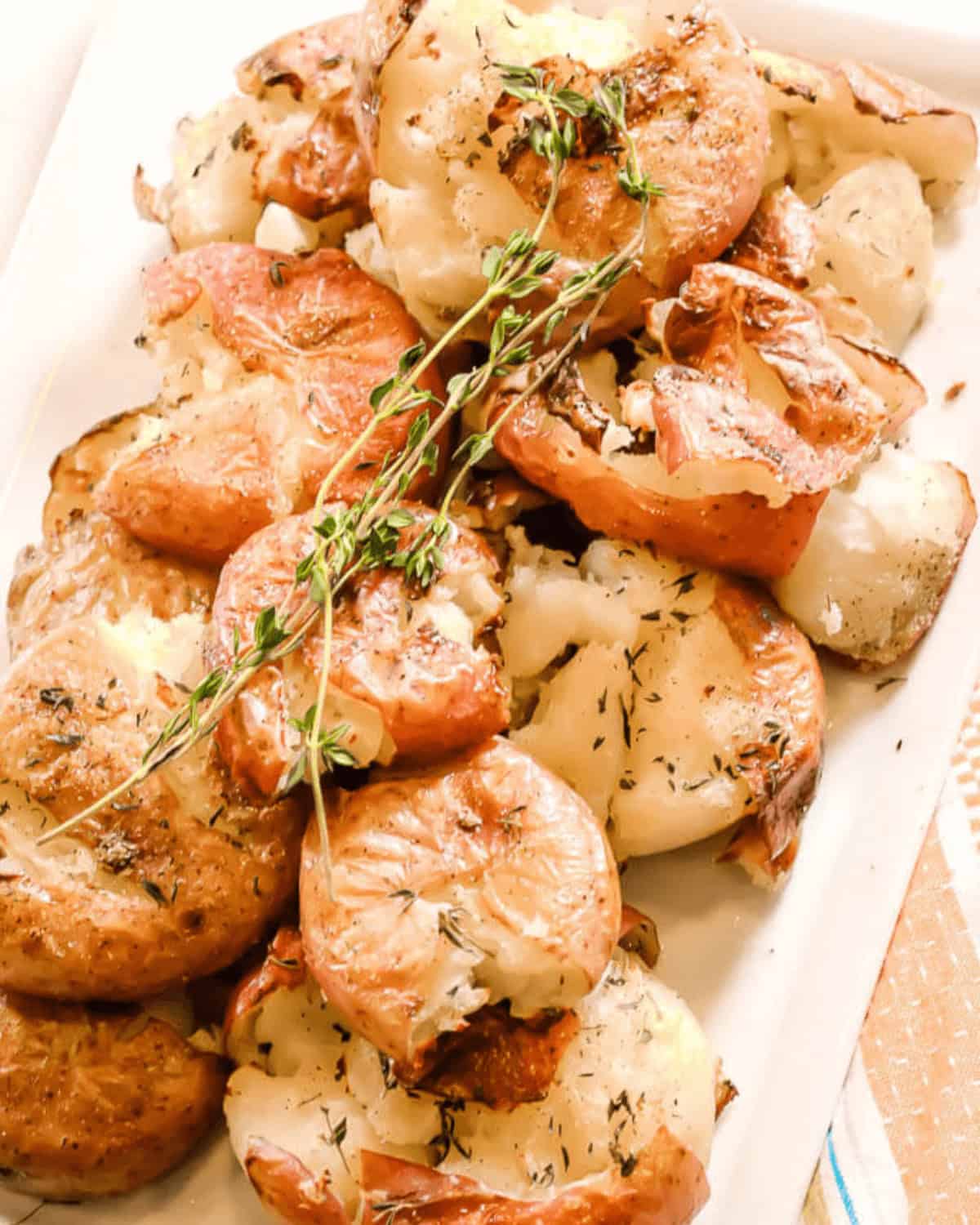A plate of roasted smashed potatoes garnished with fresh thyme, offering a crispy texture with every bite.