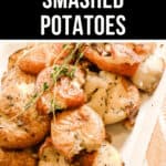 A plate of roasted smashed potatoes garnished with fresh rosemary, viewed from a slightly elevated angle. A black banner at the top of the image proudly displays the text "Roasted Smashed Potatoes.