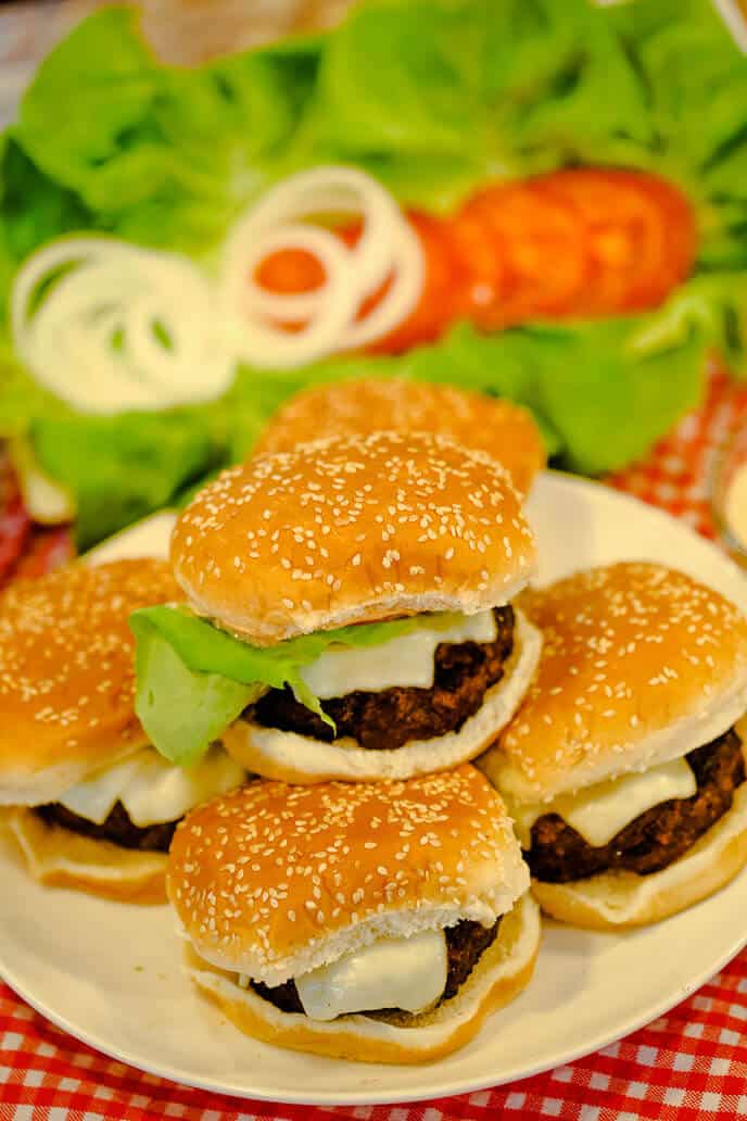 homemade burger recipe on buns with lettuce and tomatoes in background
