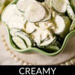 A green bowl filled with creamy cucumber onion salad. The image features text at the bottom that reads, "Creamy Cucumber Onion Salad." The background is slightly blurred, highlighting the fresh ingredients of the cucumber onion salad.