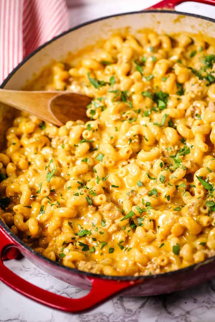 Veal cheeseburger macaroni in a red skillet with a wooden spoon