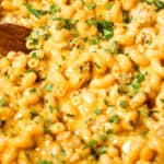 A close-up of creamy cheeseburger macaroni sprinkled with fresh herbs, with a wooden spoon partially visible on the left side of the dish.