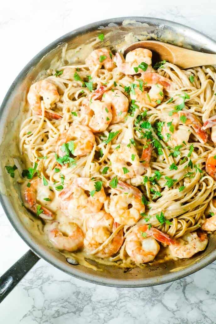 shrimp alfredo recipe in a skillet with wooden spoon on a marble table. 