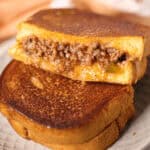 A Sloppy Joe Grilled Cheese sandwich, brimming with melted cheese and savory ground beef filling, is expertly grilled, cut in half, and elegantly stacked on a plate.