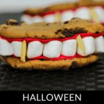 Vampire cookies with marshmallow teeth and almond sliver fangs are designed to look like eerie vampire mouths, set against a black surface.