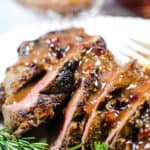 beef tenderloin recipe on a white platter with rosemary sprigs
