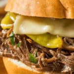 Enjoy a delightful Mississippi Pot Roast sandwich featuring shredded beef, melted cheese, and pickles nestled in a bun.
