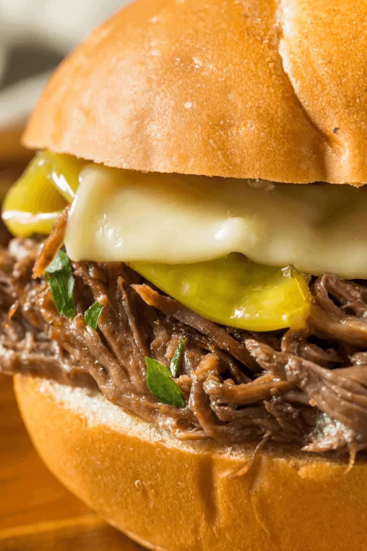 Enjoy a delightful Mississippi Pot Roast sandwich featuring shredded beef, melted cheese, and pickles nestled in a bun.