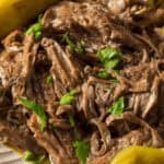Shredded beef garnished with parsley, reminiscent of a classic Mississippi Pot Roast, served with peppers and roasted vegetables on a white plate.