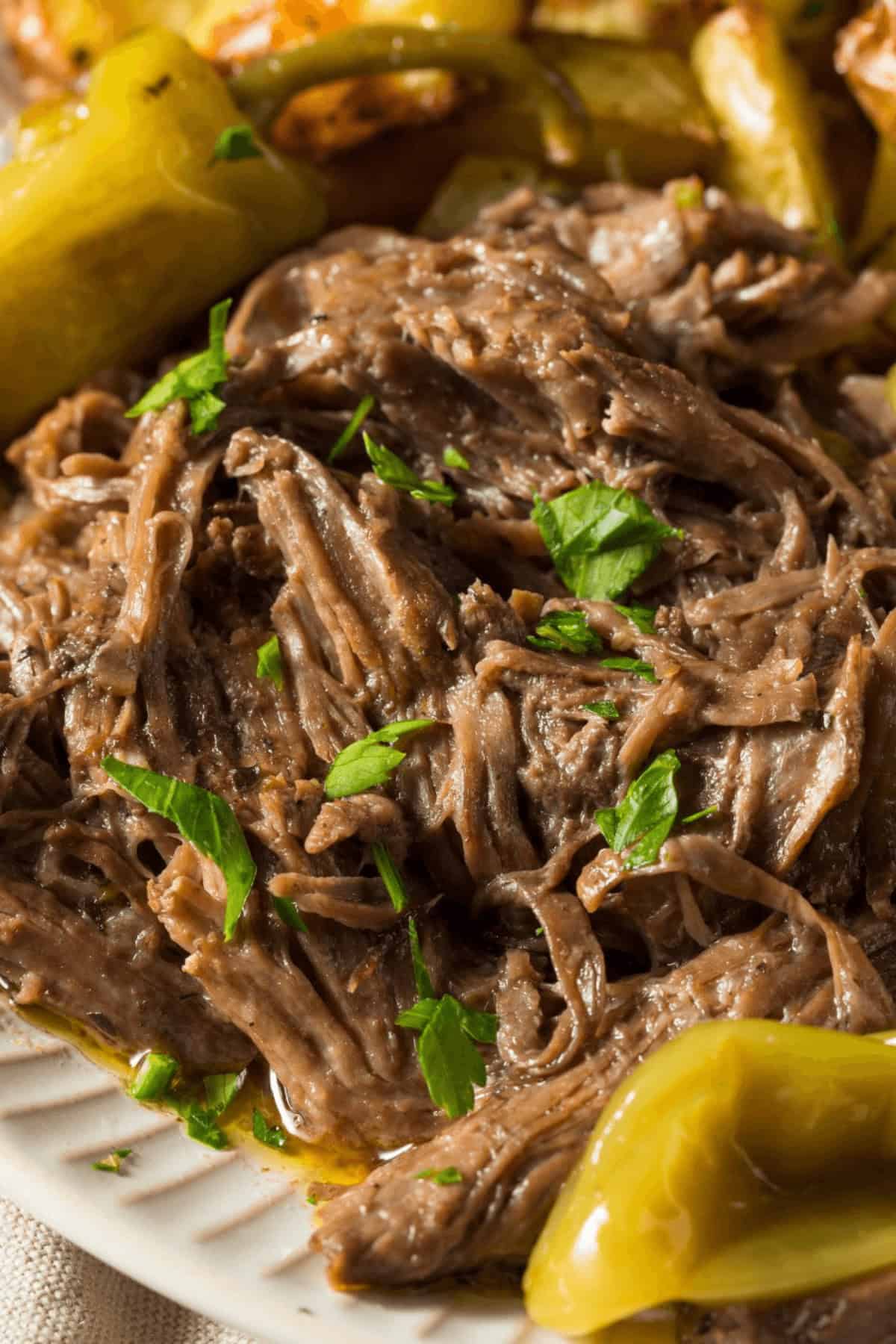 Shredded beef garnished with parsley, reminiscent of a classic Mississippi Pot Roast, served with peppers and roasted vegetables on a white plate.