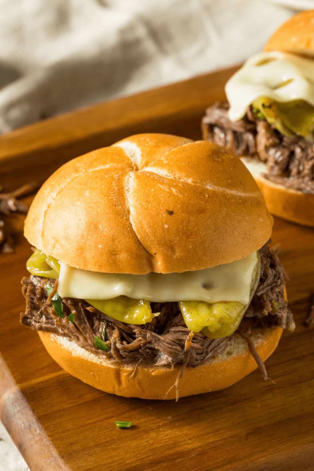 A Mississippi Pot Roast sandwich with shredded beef, melted cheese, and pickles on a bun, placed on a wooden board.