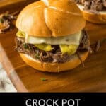 A wooden tray cradles two delectable Mississippi Pot Roast sandwiches, adorned with tangy pickles and melted cheese.