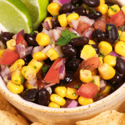 A bowl of Black Bean and Corn Salsa, garnished with lime wedges, accompanied by tortilla chips.