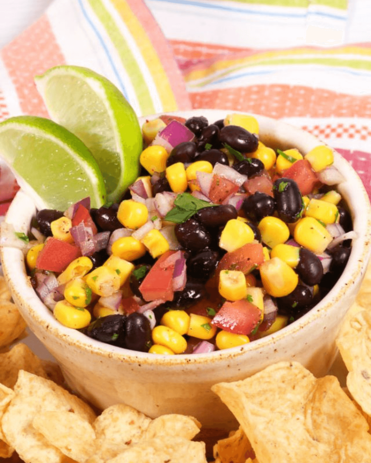 A bowl of Black Bean and Corn Salsa garnished with lime, surrounded by tortilla chips.