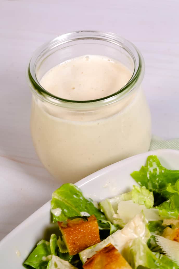 Homemade caesar salad dressing recipe in a jar with salad off to the side.