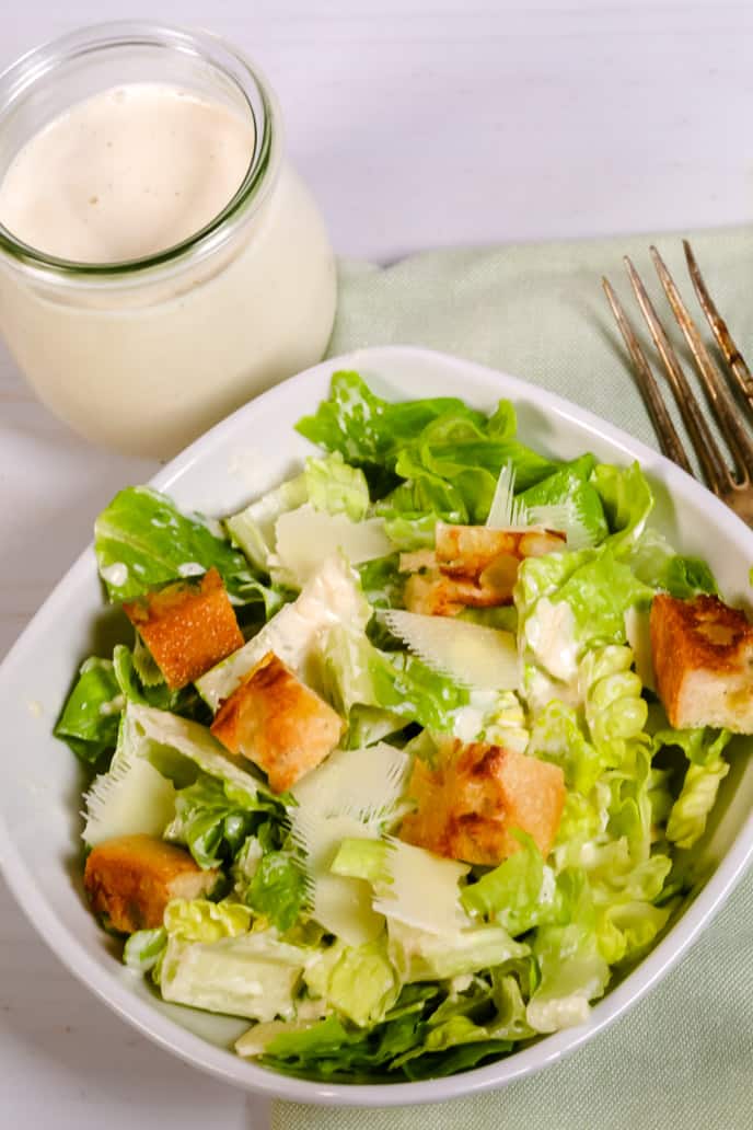 Caesar Salad in a white bowl with extra caesar salad dressing on the side
