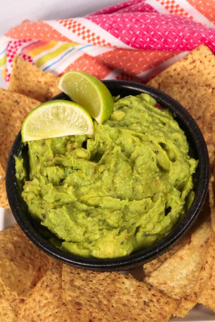 Homemade guacamole recipe in a bowl with limes and chips