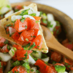 A bowl of Pico de Gallo, a Mexican salsa, on a wooden spoon.