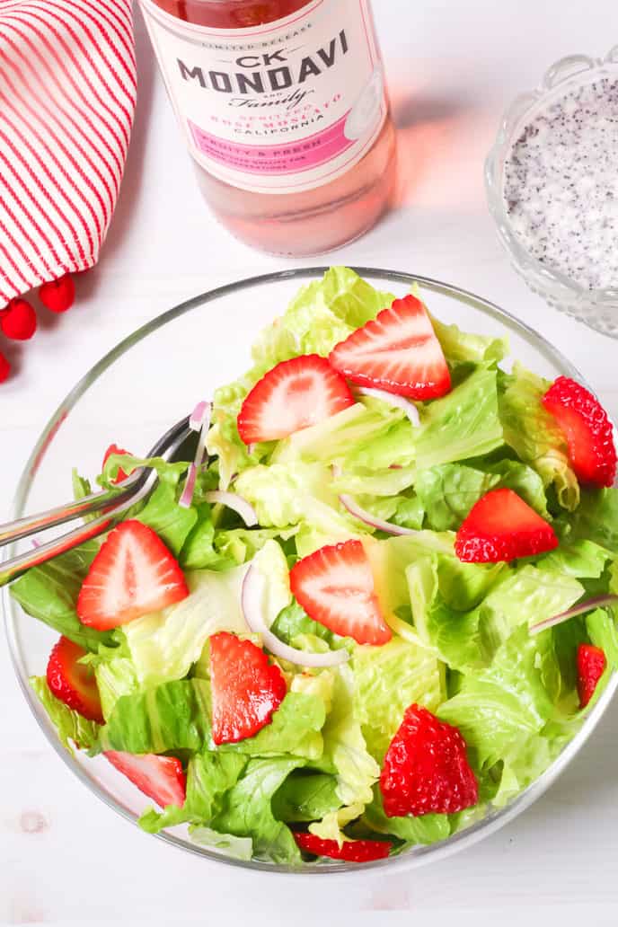 Strawberry Salad recipe with homemade poppyseed dressing in a bowl with a bottle of wine and extra dressing in the background