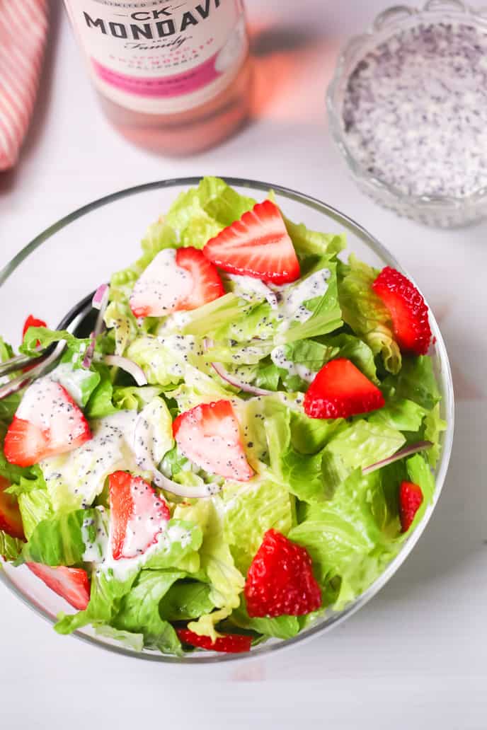 Strawberry Salad recipe with homemade poppyseed dressing in a bowl with extra dressing and a bottle of wine in the background