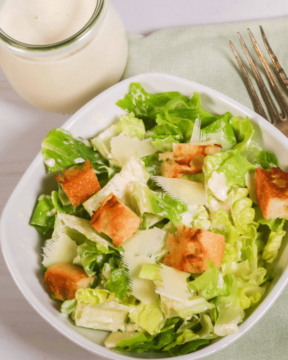 A fresh best caesar salad with croutons and shaved parmesan cheese, accompanied by a jar of dressing.