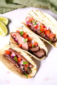 Steak Street tacos on a white plate with lime wedges.