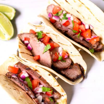 Steak Street tacos on a white plate with lime wedges.
