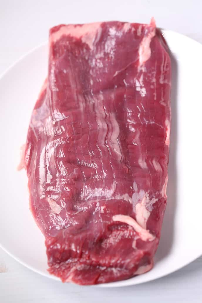 Uncooked steak on a white plate with a white background