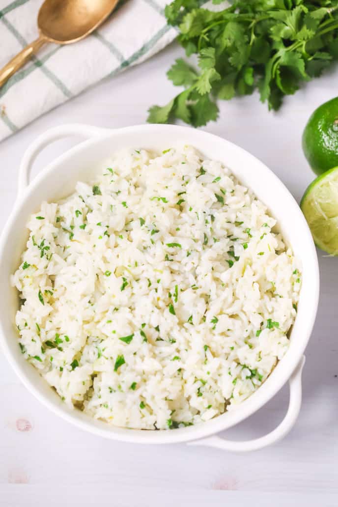 Cilantro Lime Rice in a white bowl with extra cilantro and limes on the side