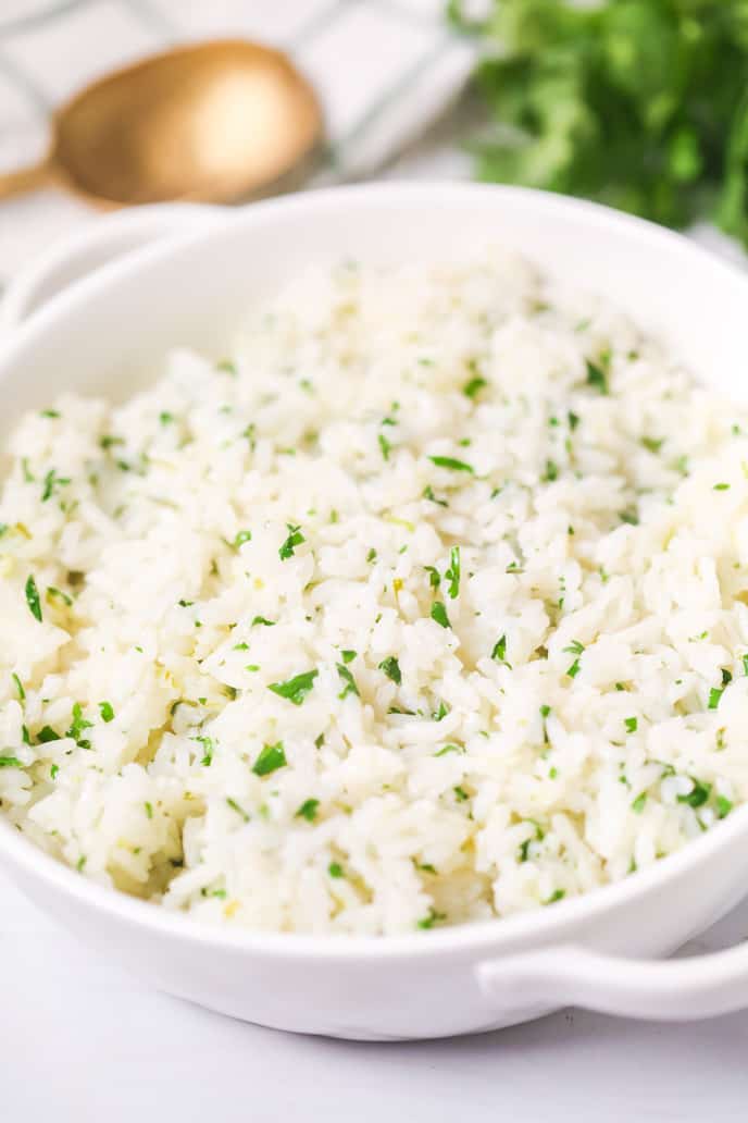 close up of Cilantro Lime Rice in a white bowl with extra cilantro and a spoon on the side