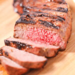 Sliced medium-rare grilled London broil on a wooden cutting board.