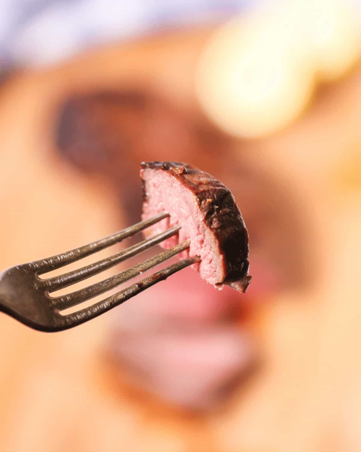 A piece of grilled, medium-rare steak on a fork with a blurred background.