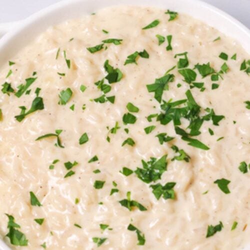 A bowl of creamy Instant Pot risotto topped with chopped green parsley on a white surface.