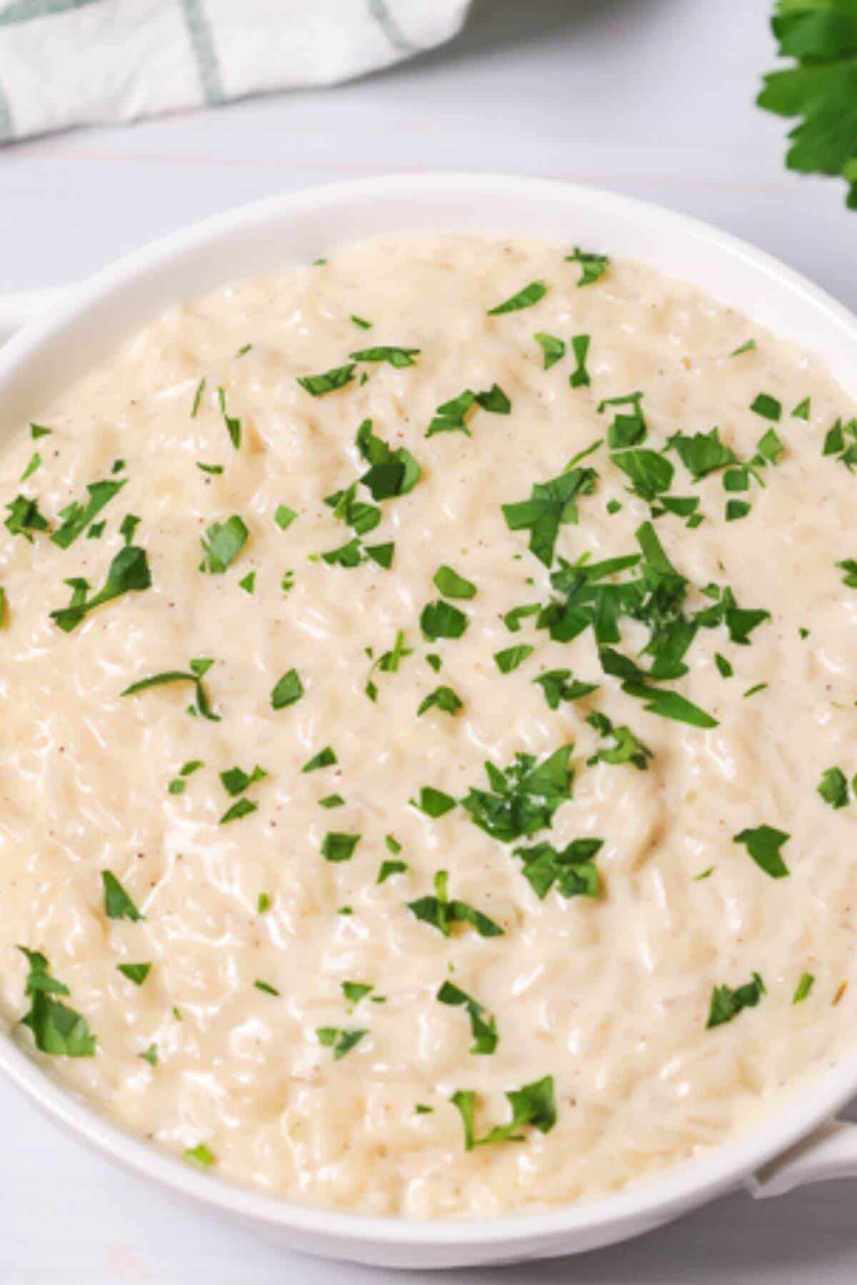 A bowl of creamy Instant Pot risotto topped with chopped green parsley on a white surface.