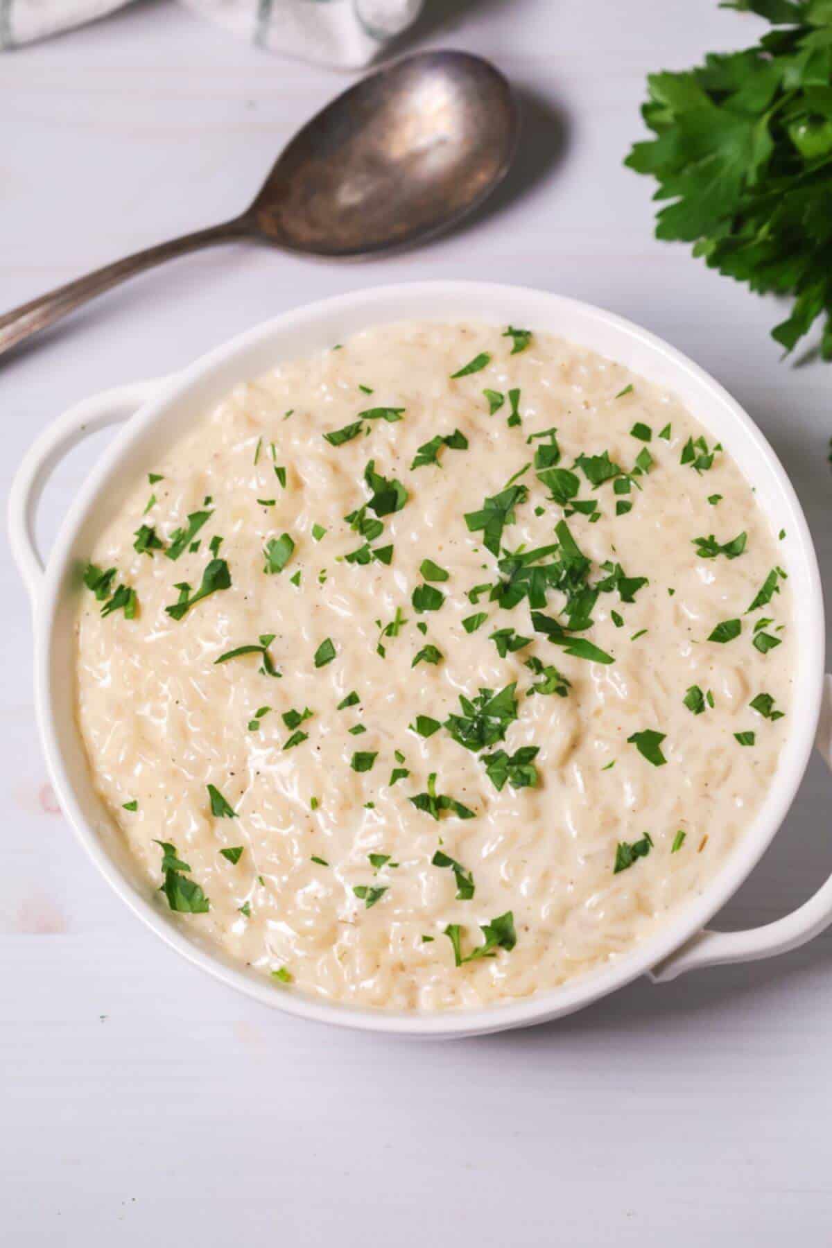 A bowl of creamy Instant Pot risotto garnished with chopped parsley, placed on a light surface. A spoon and some parsley leaves are in the background.
