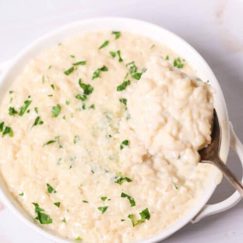 A bowl of creamy side dish topped with chopped parsley, with a spoon elegantly lifting a portion from the side.